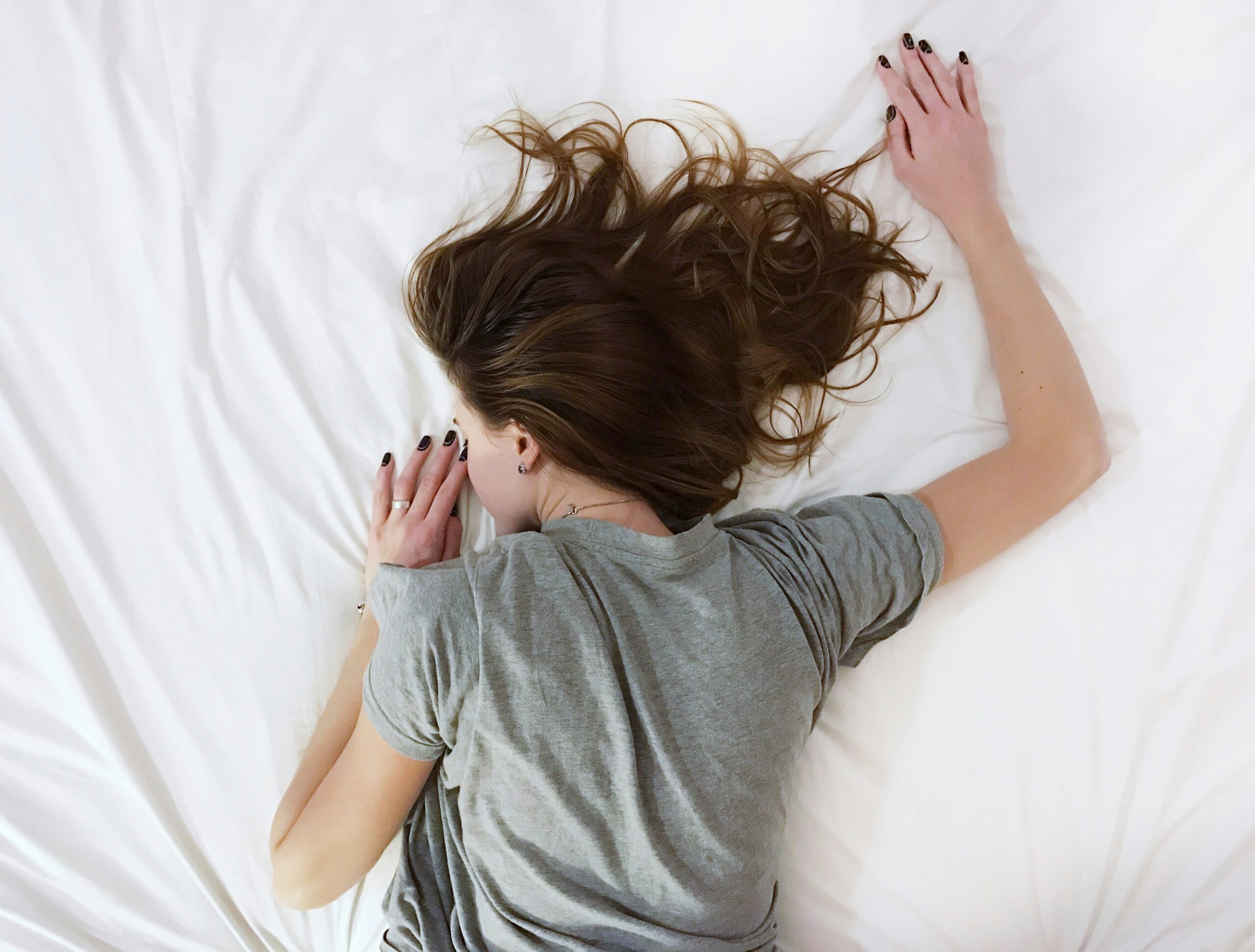 exhausted woman lying on a bed with white sheets to depict adrenal fatigue