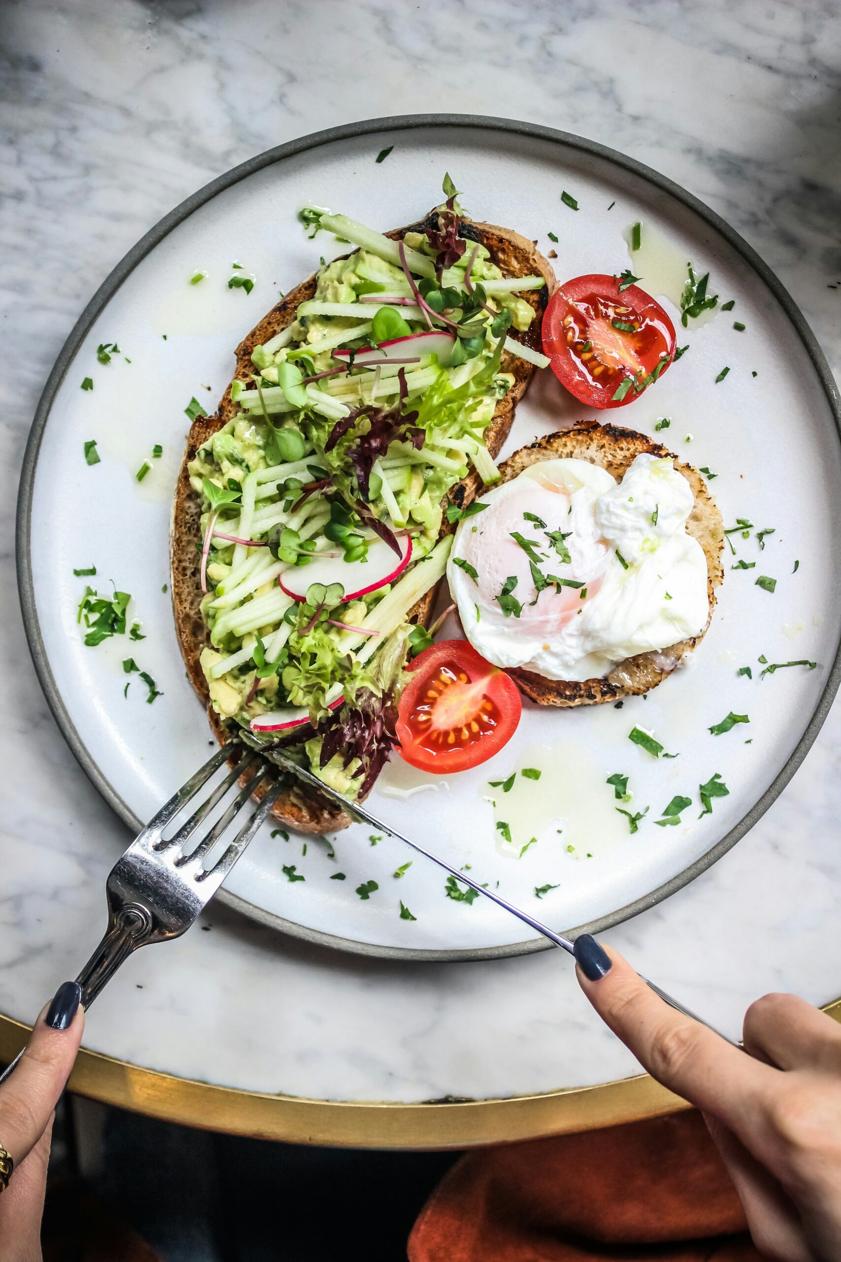 white pottery plate with avocado toast, cherry tomatoes, and poached egg with fork and knife cutting into it to illustrate berberine working like metformin when taken with meals