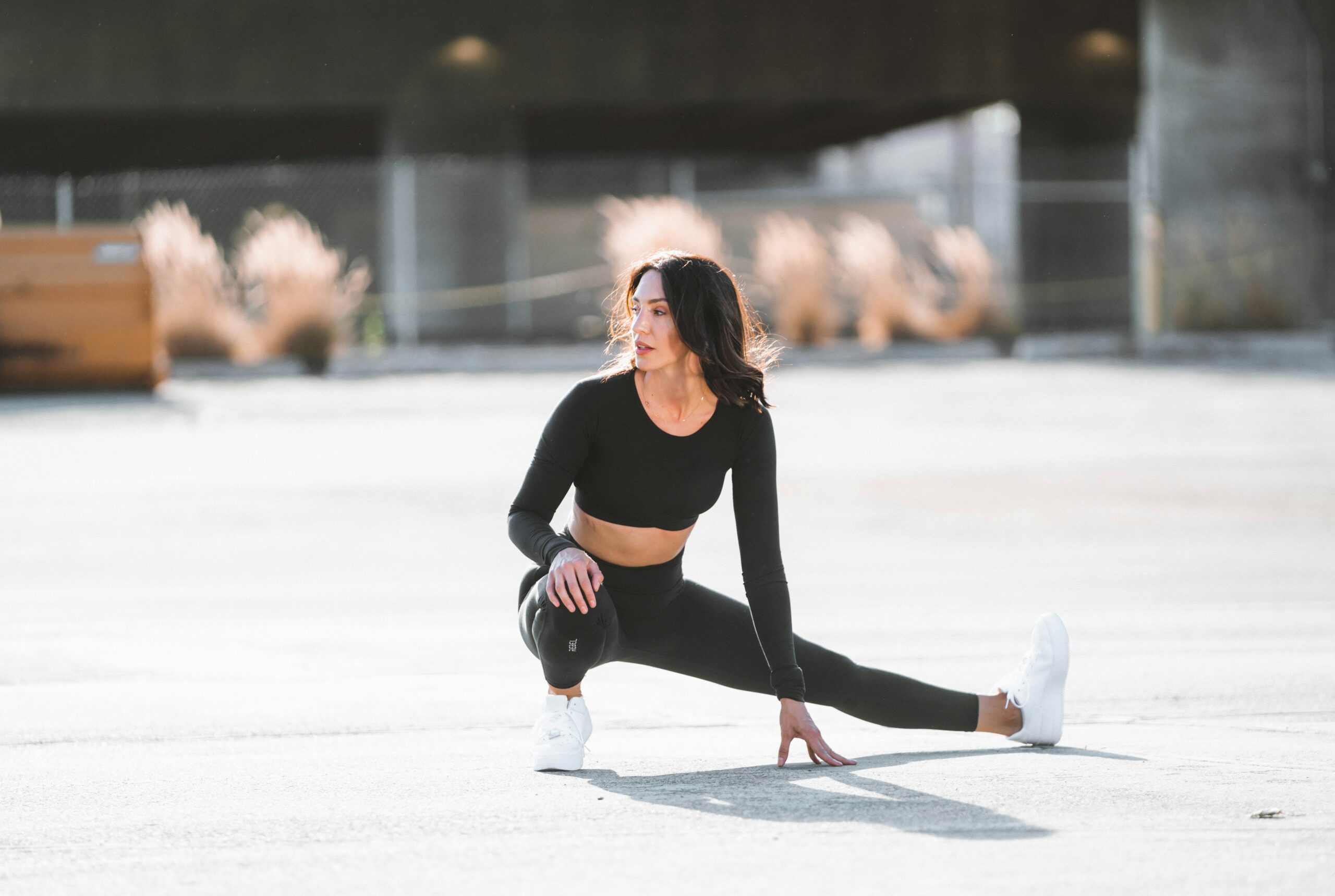 woman stretching on concrete wearing black activewear and white sneakers